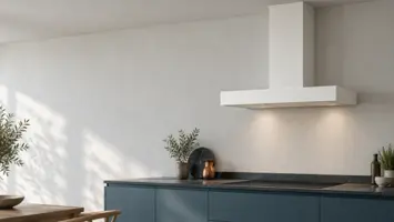 Hvid væghængt skorstensemhætte på en pudset væg over en mørk bordplade med kogeplade